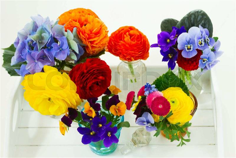 Set of colorful freshly cut flowers in glass vases on white wooden table, stock photo
