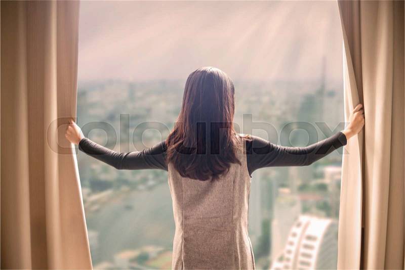 Asian portrait beautiful woman opening curtains and building cityscape background, stock photo