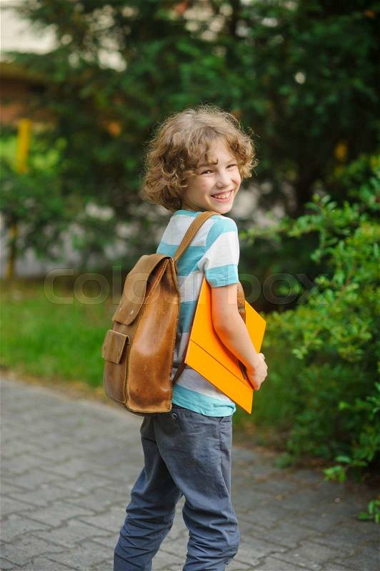 The pupil with a school backpack behind the back. The school student stand in a half-turn to the camera. He looks in a camera and smiles. In hands - the yellow folder, stock photo