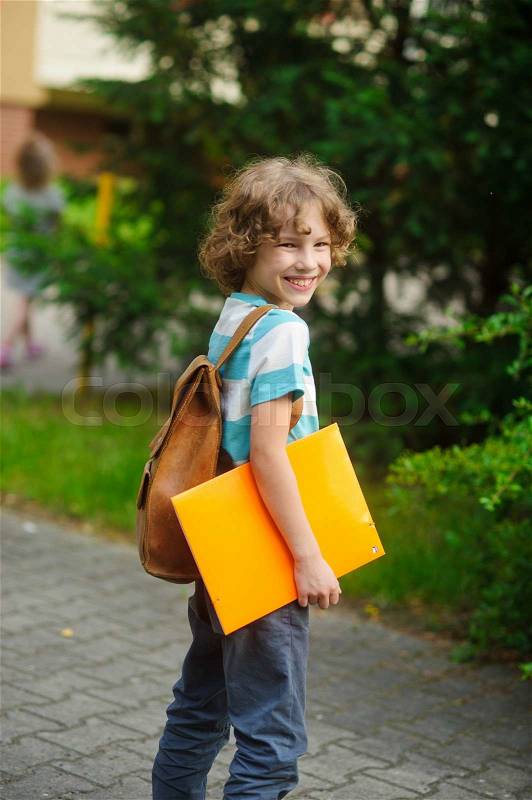 The pupil with a school backpack behind the back. The school student stand in a half-turn to the camera. He looks in a camera and smiles. In hands - the yellow folder, stock photo