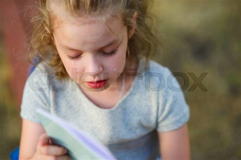 The little schoolgirl cries over a school notebook. The schoolgirl on cheeks has tears. The girl has a sad look, stock photo