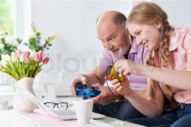Portrait of happy grandfather and little granddaughter playing video games, stock photo