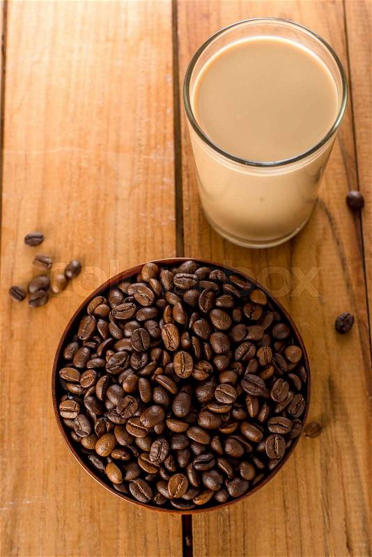 Coffee beans in bowl and a glass of coffee milk on wooden table, stock photo