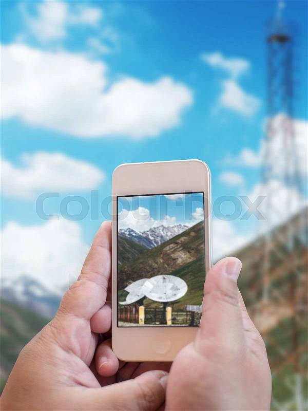 Hand holding mobile phone with Big satellite dishes antena and solar panels, energy concept, stock photo