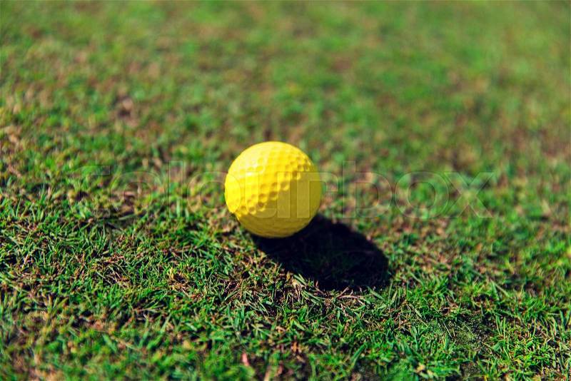 Game, entertainment, sport and leisure concept - close up of yellow golf ball on green field grass, stock photo