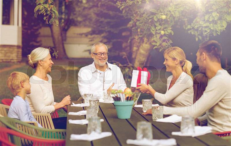 Family, happiness, generation, home and people concept - happy family with gift box having holiday dinner outdoors, stock photo
