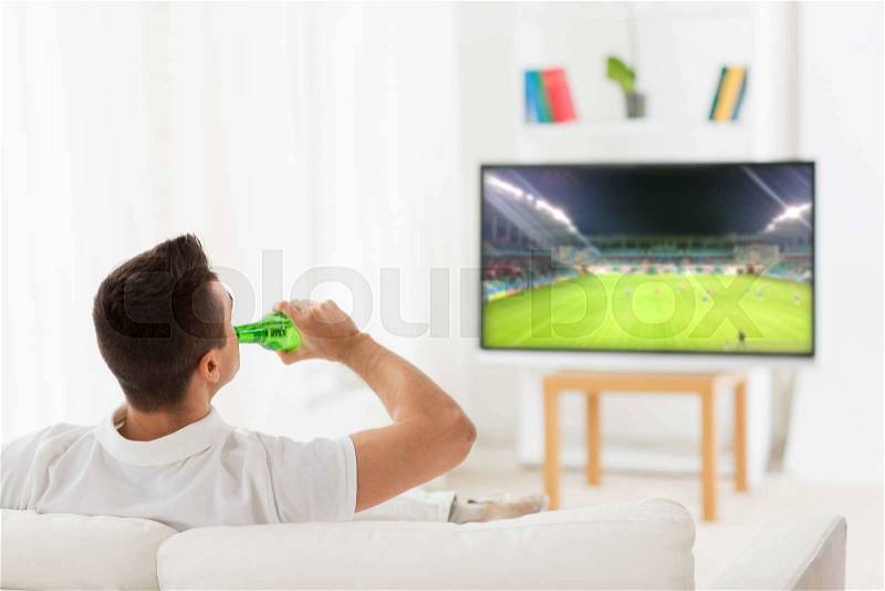 Leisure, technology, mass media and people concept - man watching football or soccer game on tv and drinking beer from bottle at home from back, stock photo