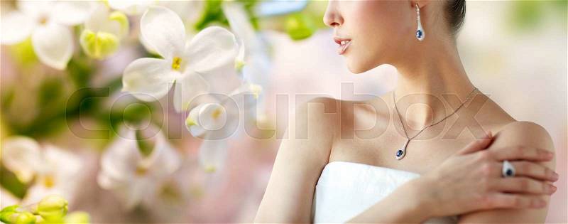 Beauty, jewelry, people and luxury concept - beautiful asian woman or bride with earring, finger ring and pendant over natural spring lilac blossom background, stock photo