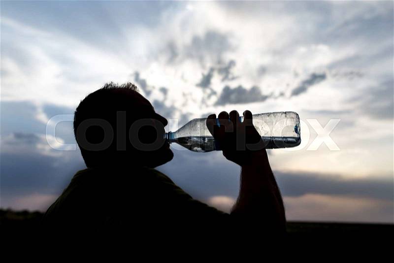 Silhouette of a man drinking water at sunset, stock photo