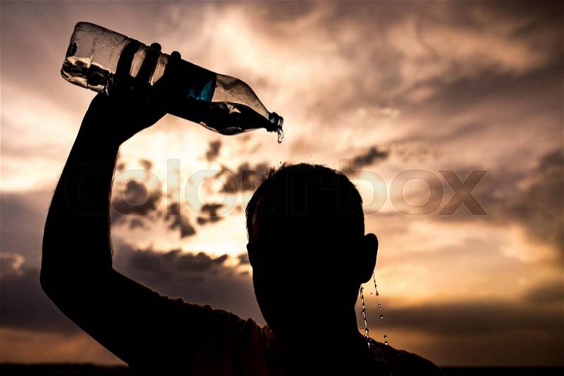 Man pours water on his head in the sunset, stock photo