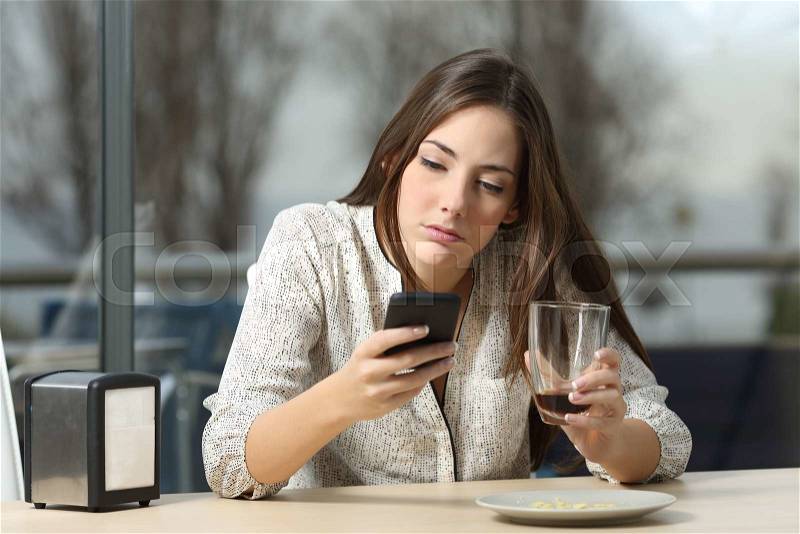 Angry woman stood up in a date in a coffee shop searching for messages and lost calls in a smart phone, stock photo