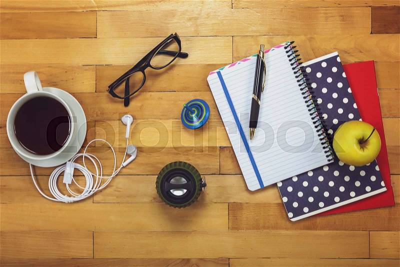 Notebooks, pen, glasses, music speakers, headphones, mobile phone, cup of tea, apple on a wooden background, stock photo
