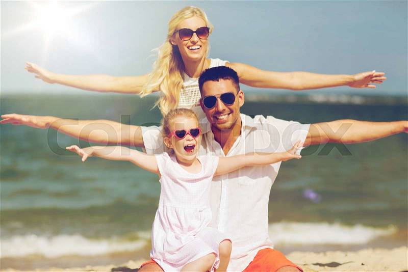 Family, vacation, adoption and people concept - happy man, woman and little girl in sunglasses having fun on summer beach, stock photo