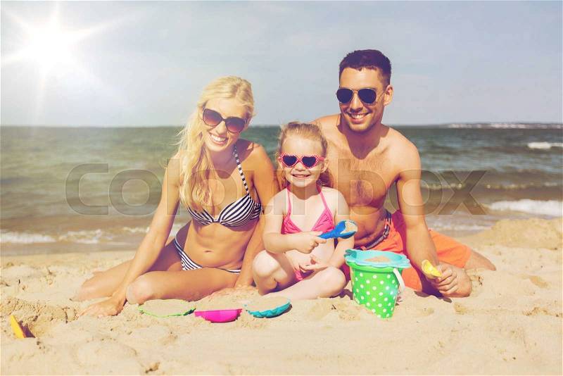 Family, travel, vacation and people concept - happy man, woman and little girl in sunglasses playing with sand toys on summer beach, stock photo