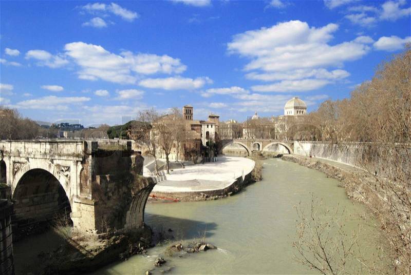Roman Island Isola Tiberina with a fragment of the ancient bridge over the turbid river Tiber with bright sky, stock photo