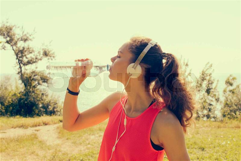 Sporty Girl with headphones and a red t-shirt drinking water from a bottle, yellow toning, stock photo