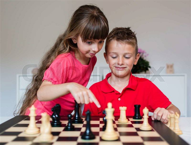 Girl helping boy while playing a game of chess on large chess board, stock photo