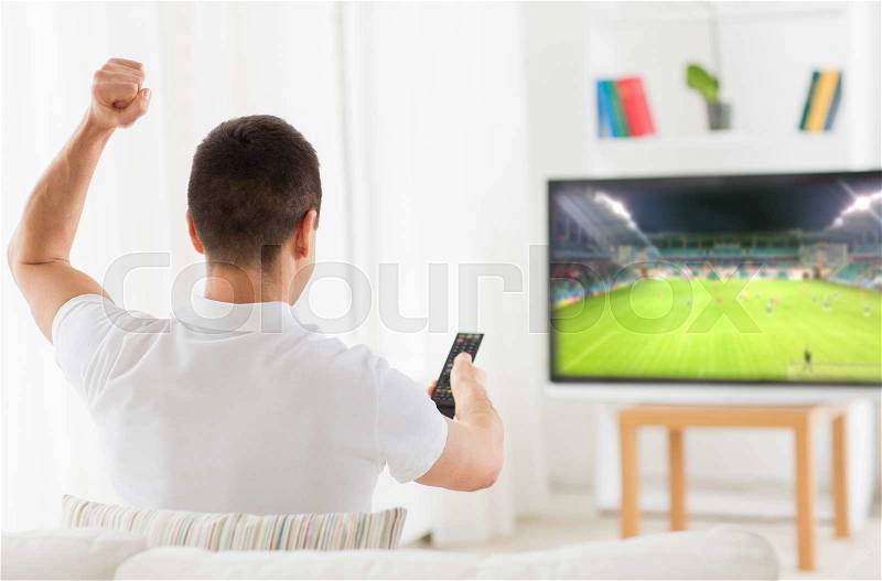 Leisure, technology, mass media and people concept - happy man watching football or soccer game on tv and supporting team at home from back, stock photo