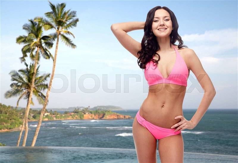 People, fashion, swimwear, summer and travel concept - happy young woman posing in pink bikini swimsuit over Sri Lanka beach with palms swimming pool background, stock photo