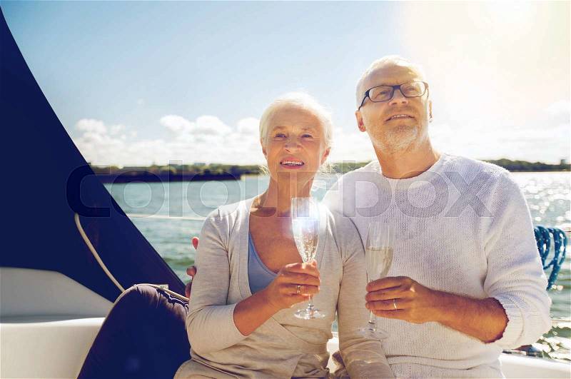 Sailing, age, travel, holidays and people concept - happy senior couple with champagne glasses on sail boat or yacht deck floating in sea, stock photo
