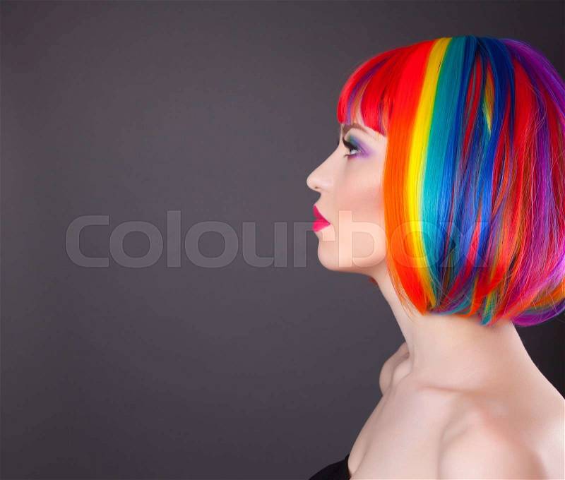 Beautiful woman wearing colorful wig and showing colorful nails against gray background, stock photo