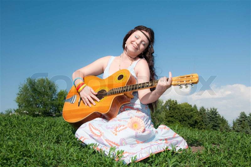Beautiful young hippie girl with a guitar sitting on green grass and sings songs, stock photo