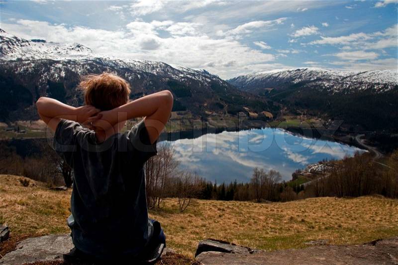 A boy folding his arms behind his head. Sitting on a top of a mountain watching the view, stock photo