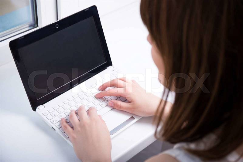 Back view of young woman using laptop with blank screen, stock photo