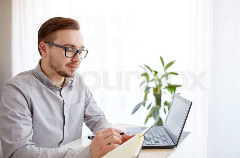 Business, startup and people concept - businessman or creative male worker writing to notebook or diary with pen at home office, stock photo