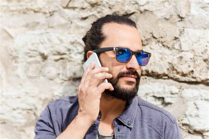 Leisure, technology, communication and people concept - man calling on smartphone on street at stone wall, stock photo