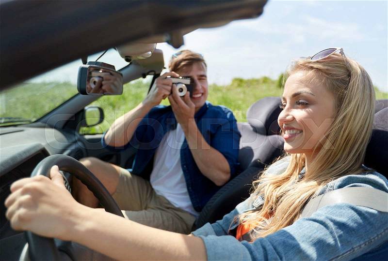 Leisure, road trip, travel and people concept - happy couple driving in cabriolet car and taking picture by film camera, stock photo