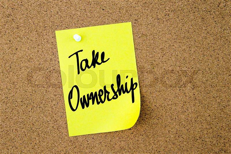 Take Ownership written on yellow paper note pinned on cork board with white thumbtacks, copy space available, stock photo