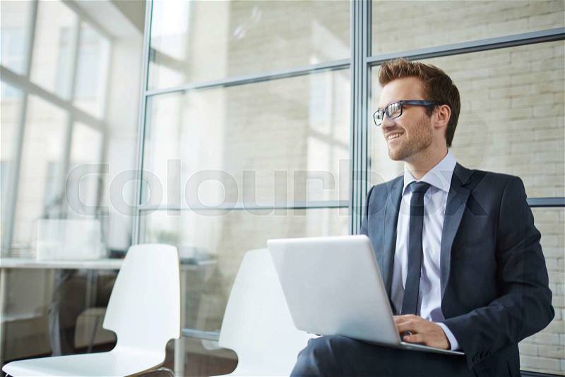 Businessman sitting with laptop in office and smiling, stock photo