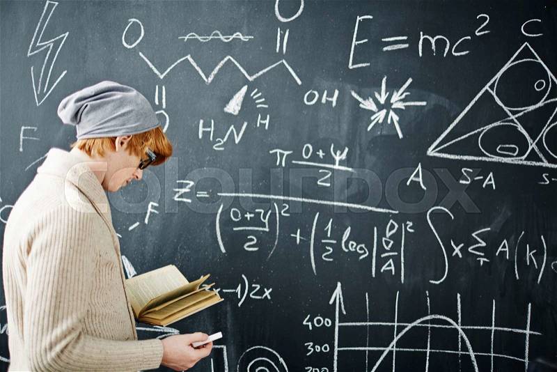 Student with open book and piece of chalk standing by blackboard, stock photo