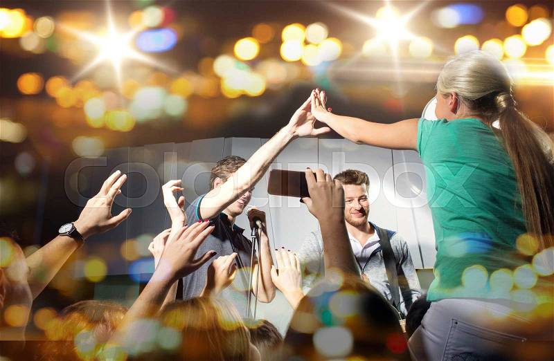 Holidays, music, gesture, nightlife and people concept - close up of woman fan making high five with singer at concert in night club, stock photo