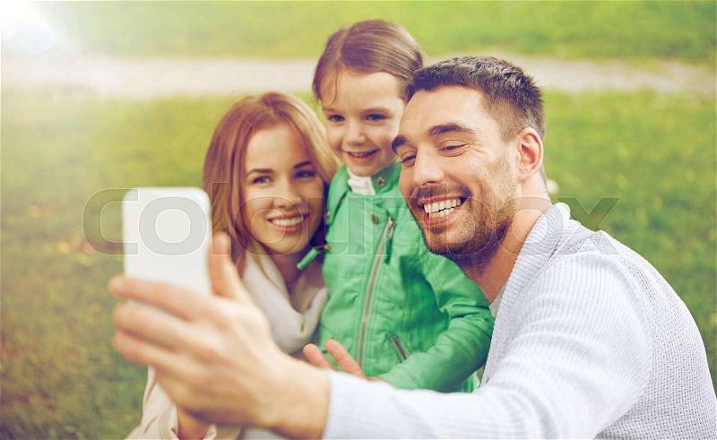 Family, childhood, technology and people concept - happy father, mother and little daughter taking selfie by smartphone in park, stock photo