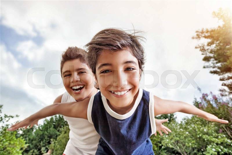 Happy brothers having fun outdoors, playing as if flying, two active boys spending summer holidays with pleasure in a countryside, stock photo