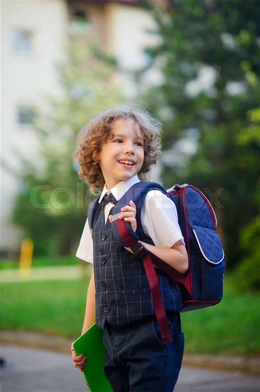 The primary school students standing in the school yard. Little schoolboy smartly dressed. Behind the boy\'s school backpack. The first grader looks away and smiles. Back to school, stock photo