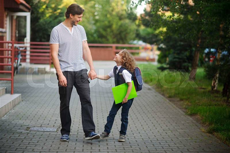 Dad walks to school his son. The tall man holds the hand of a little schoolboy. Father and son with love and tenderness look at each other. The boy is smartly dressed. Back to school, stock photo