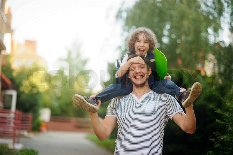 Little schoolboy sitting on the shoulders of his father. The father holds the boy\'s legs. The boy delighted. He likes to joke with dad. Father and son smiling happily. Back to school, stock photo