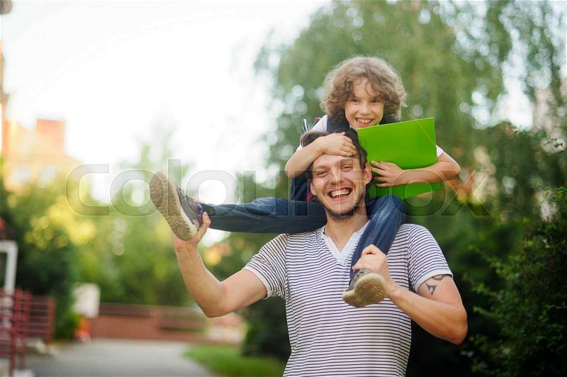 Little schoolboy sitting on the shoulders of his father and clings to his head. The father holds the boy\'s legs. The boy delighted. He likes to joke with dad. Father and son smiling happily. Back to school, stock photo