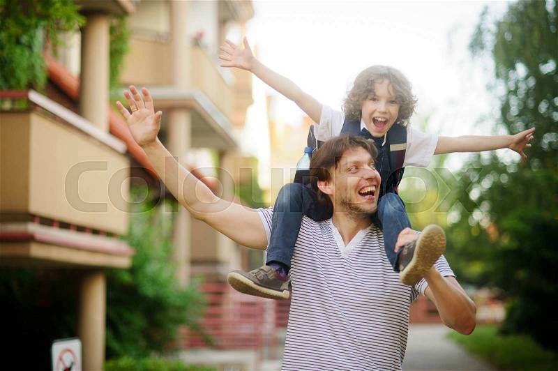 First grader sitting on the shoulders of his father. He is very happy. Father and son pretending to fly. They have a good mood, stock photo