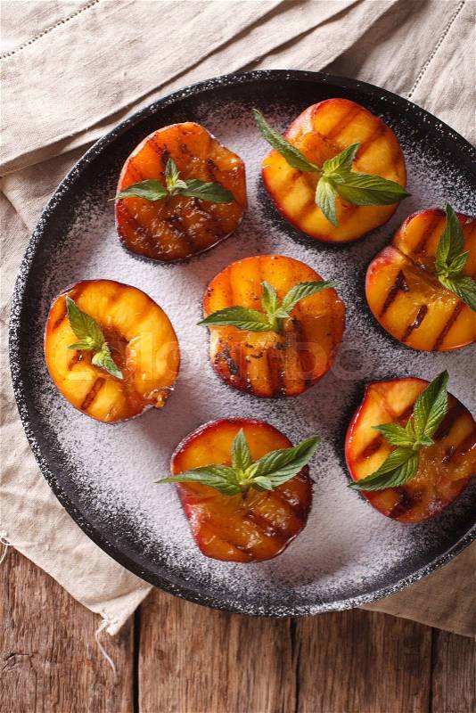 Healthy Dessert: grilled Peaches with powdered sugar and mint close-up on a plate on the table. Vertical view from above\, stock photo