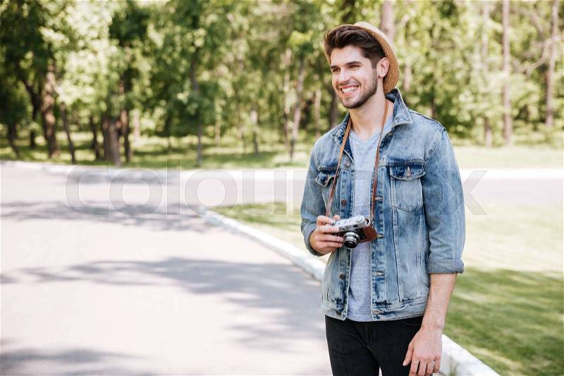 Happy atttractive young man in hat with old vintage photo camera outdoors, stock photo