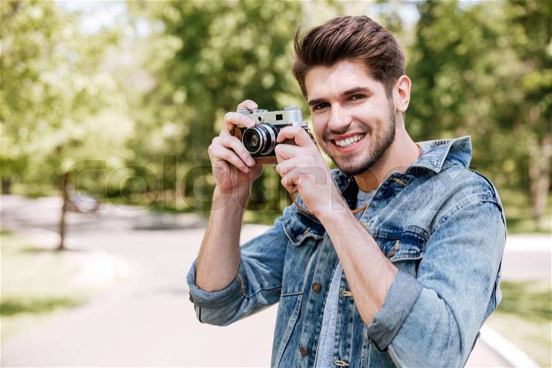 Happy casual hipster man making photo using retro camera outdoors in the park, stock photo