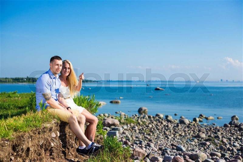 Summer vacation and travel concept - happy couple sitting on rocky beach, stock photo