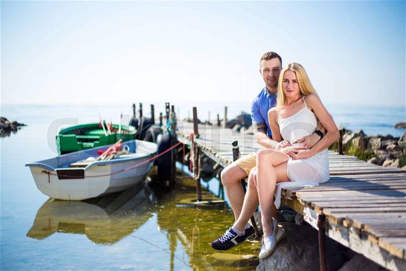 Portrait of romantic young beautiful couple sitting on old wooden pier, stock photo