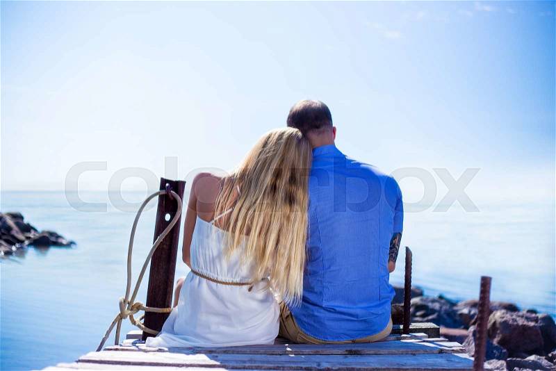 Back view of romantic young couple sitting on the pier and enjoying sea view, stock photo