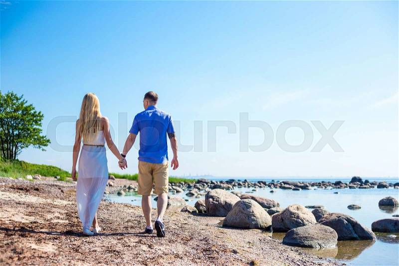 Back view of happy couple in love walking on summer beach, stock photo