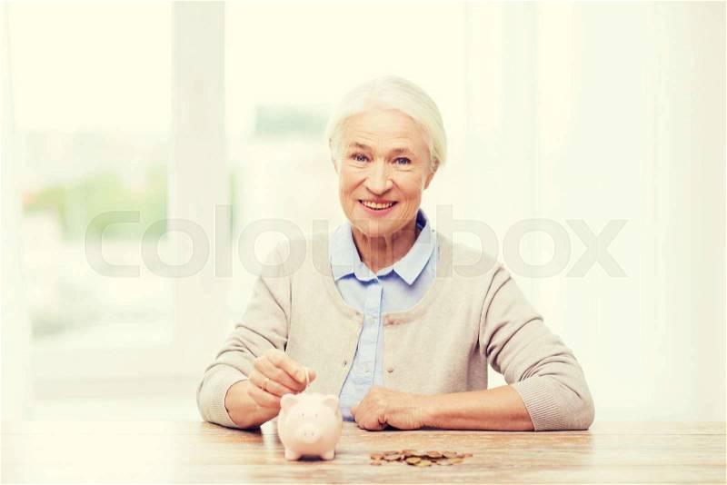 Savings, money, annuity insurance, retirement and people concept - smiling senior woman putting coins into piggy bank at home, stock photo